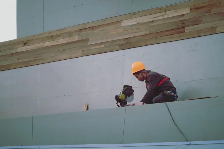 Ouvrier du bâtiment portant un casque de chantier utilisant une scie circulaire sur un chantier.