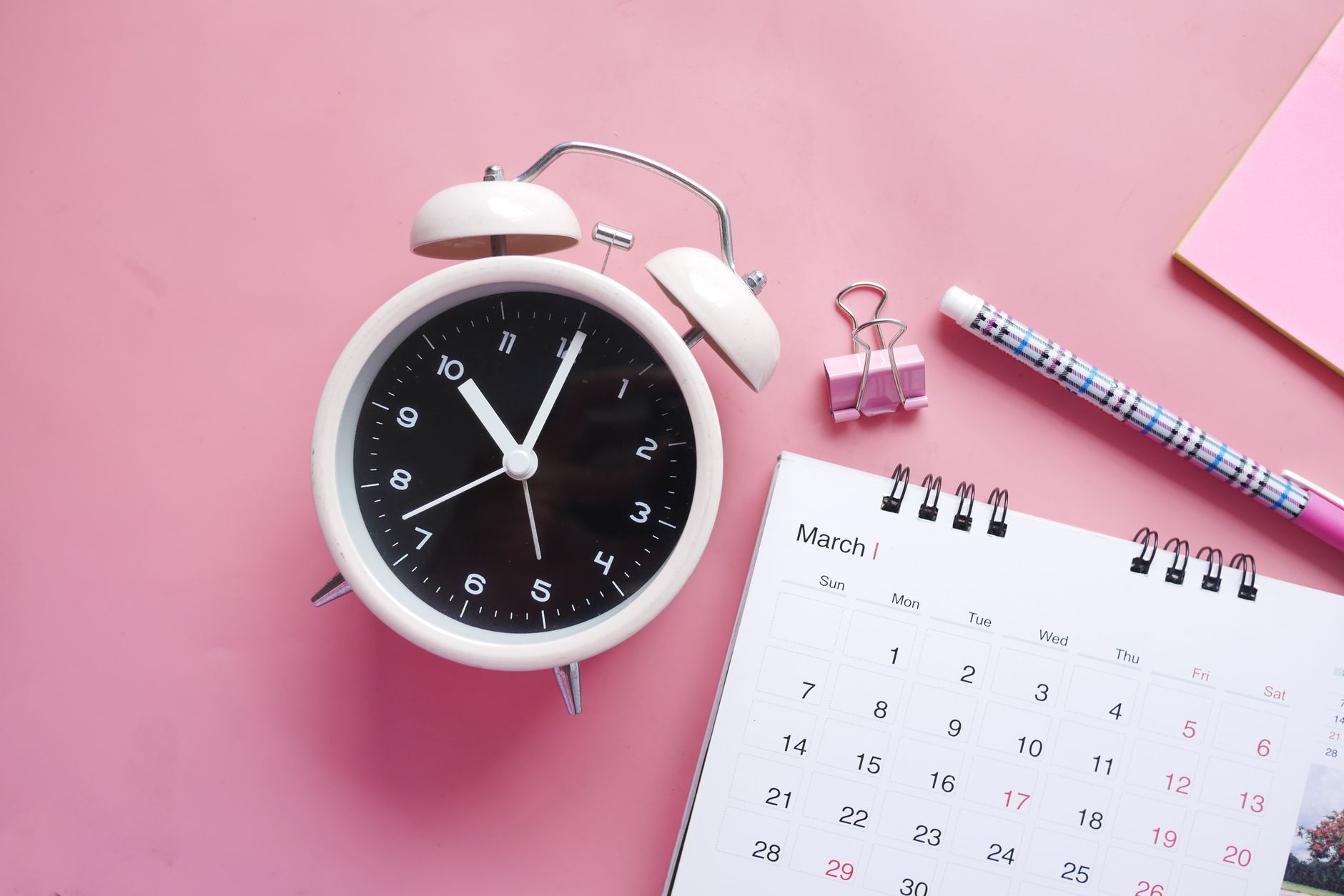 Réveil, calendrier et stylo posés sur un bureau, illustrant les délais de paiement.