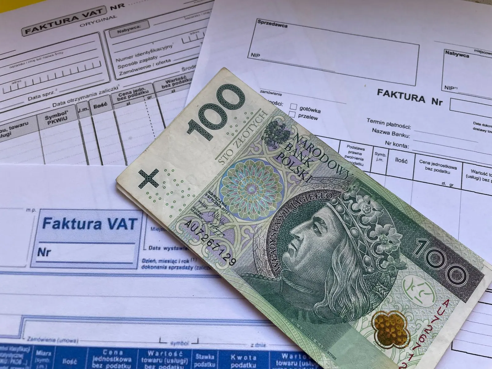 Billet de 100 Zloty polonais posé sur des factures de TVA, symbolisant la gestion de la TVA en micro-entreprise