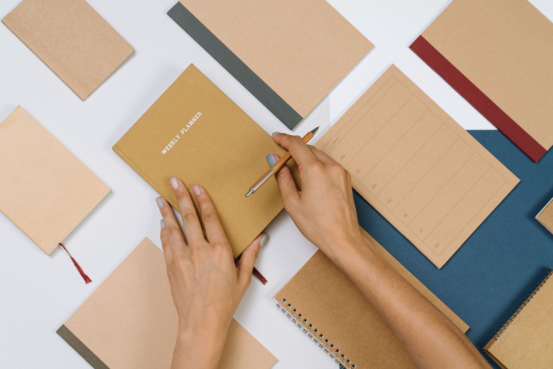 Mains remplissant un agenda hebdomadaire entouré de fournitures de bureau.
