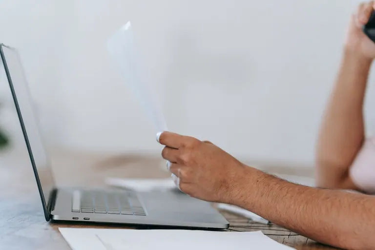 Un homme qui gère plusieurs tâches, parlant au téléphone et consultant des documents tout en travaillant sur un ordinateur