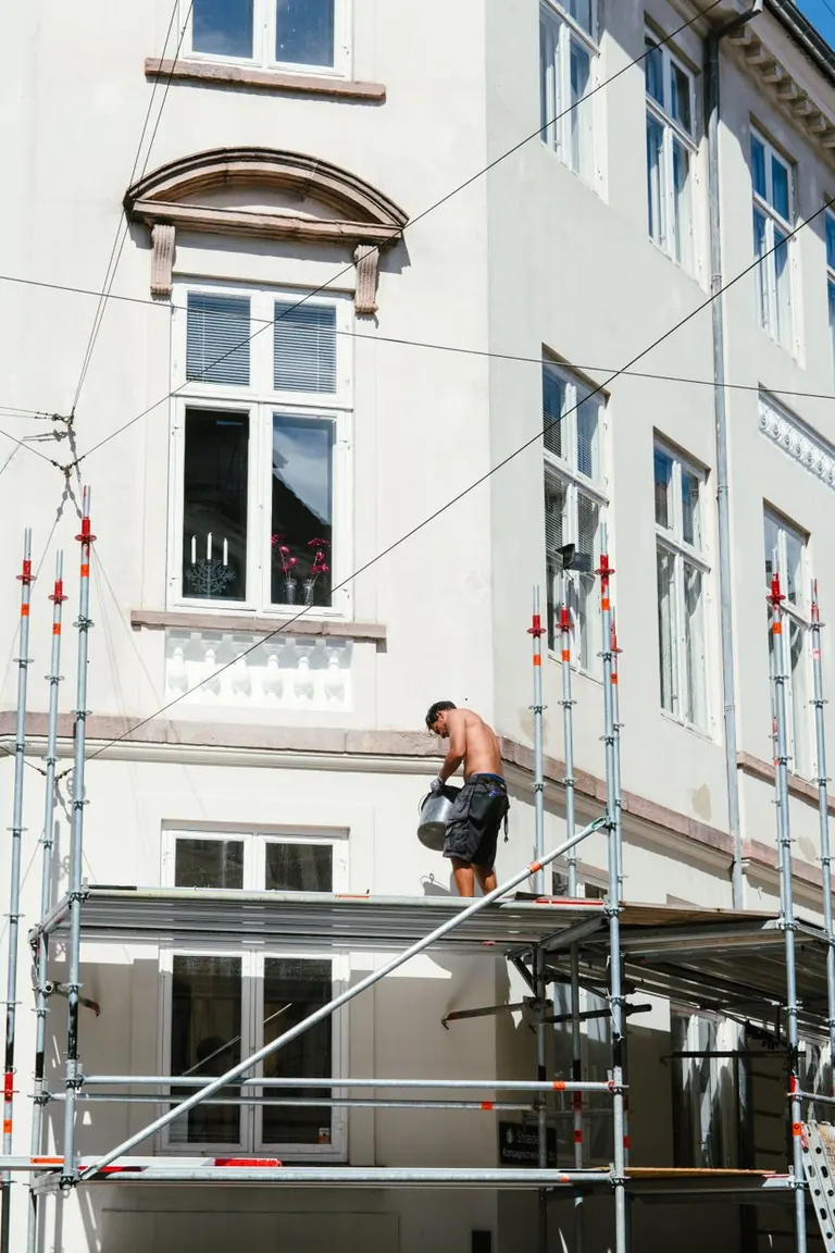 Travailleur sur un échafaudage à l'extérieur d'un bâtiment résidentiel, illustrant l'activité d'un indépendant.