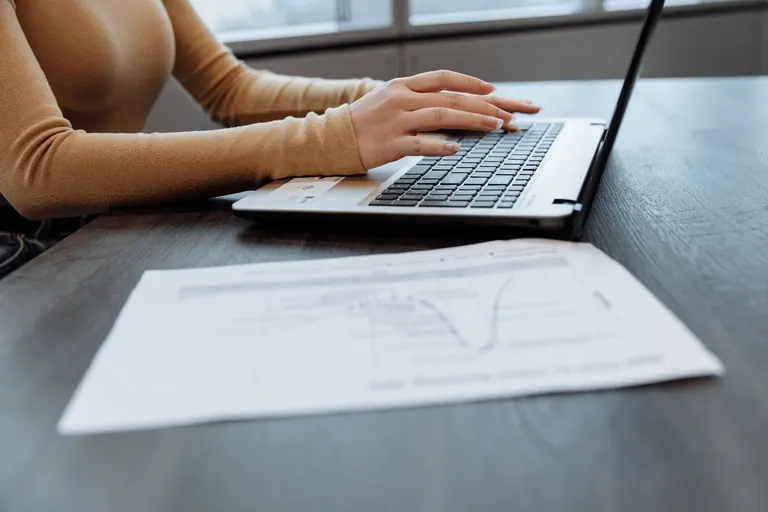 Gros plan sur les mains d'une personne tapant sur un ordinateur portable sur un bureau avec des documents. Idéal pour des