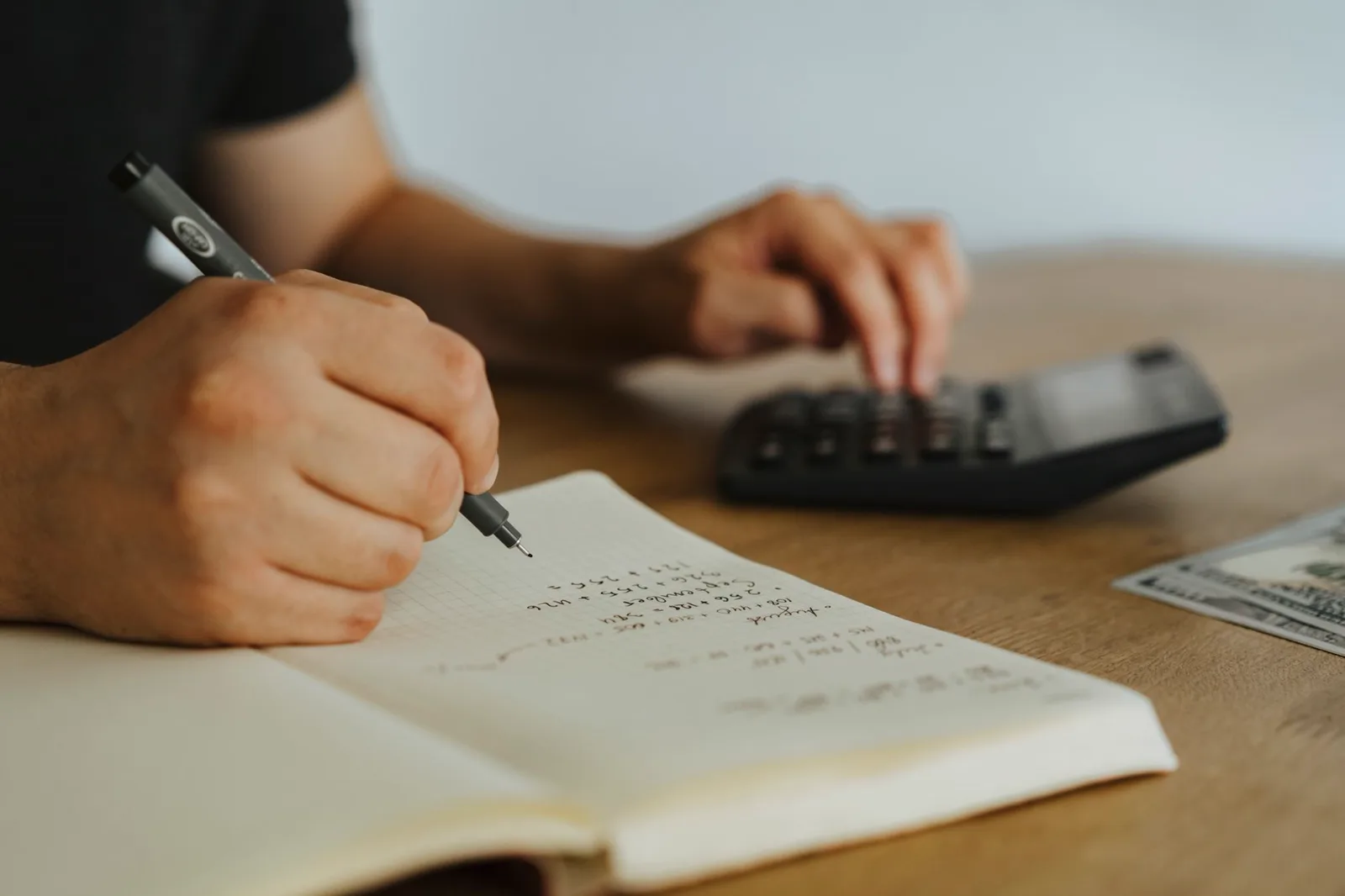 Gros plan sur des mains écrivant des calculs dans un carnet avec une calculatrice, illustrant la franchise de TVA.